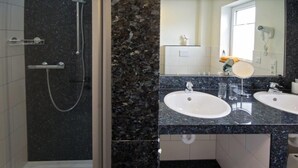 Een badkamer met een douche, twee wastafels, een spiegel en een weegschaal.
