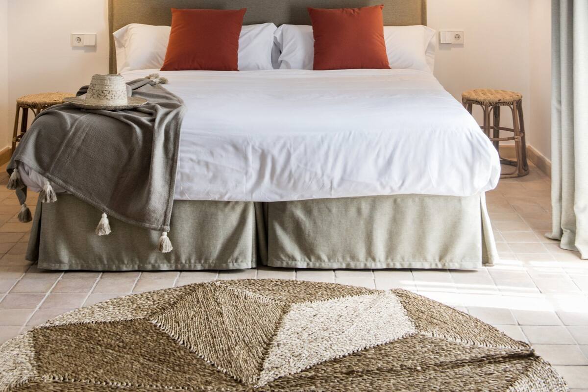 Un dormitorio con cama, dos lámparas de noche, cabecero y alfombra de fibras naturales.