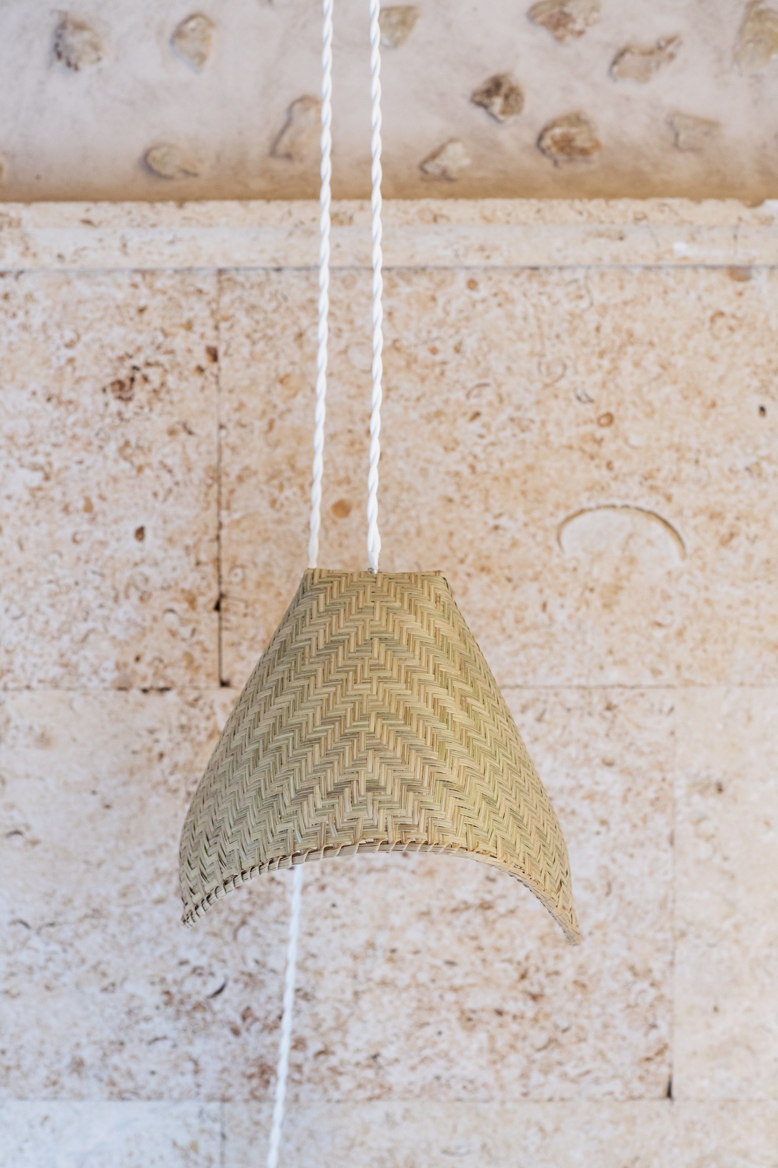 Uma luminária suspensa, trançada, com padrão em zigue-zague, pendurada por cordas brancas.