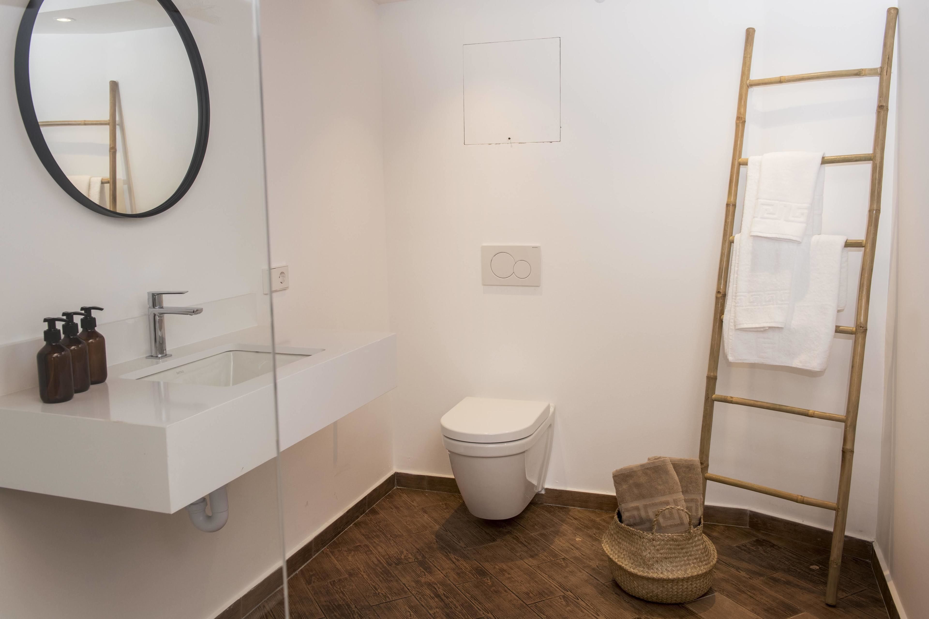 Un baño moderno con un lavamanos blanco, espejo, inodoro y una escalera de madera con toallas.