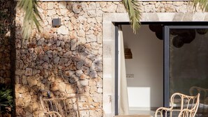 Un muro de piedra con una palmera, una puerta de cristal y muebles de mimbre.