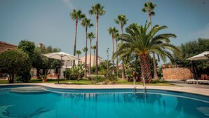 Una piscina rodeada de palmeras y sombrillas, bajo un cielo azul despejado.