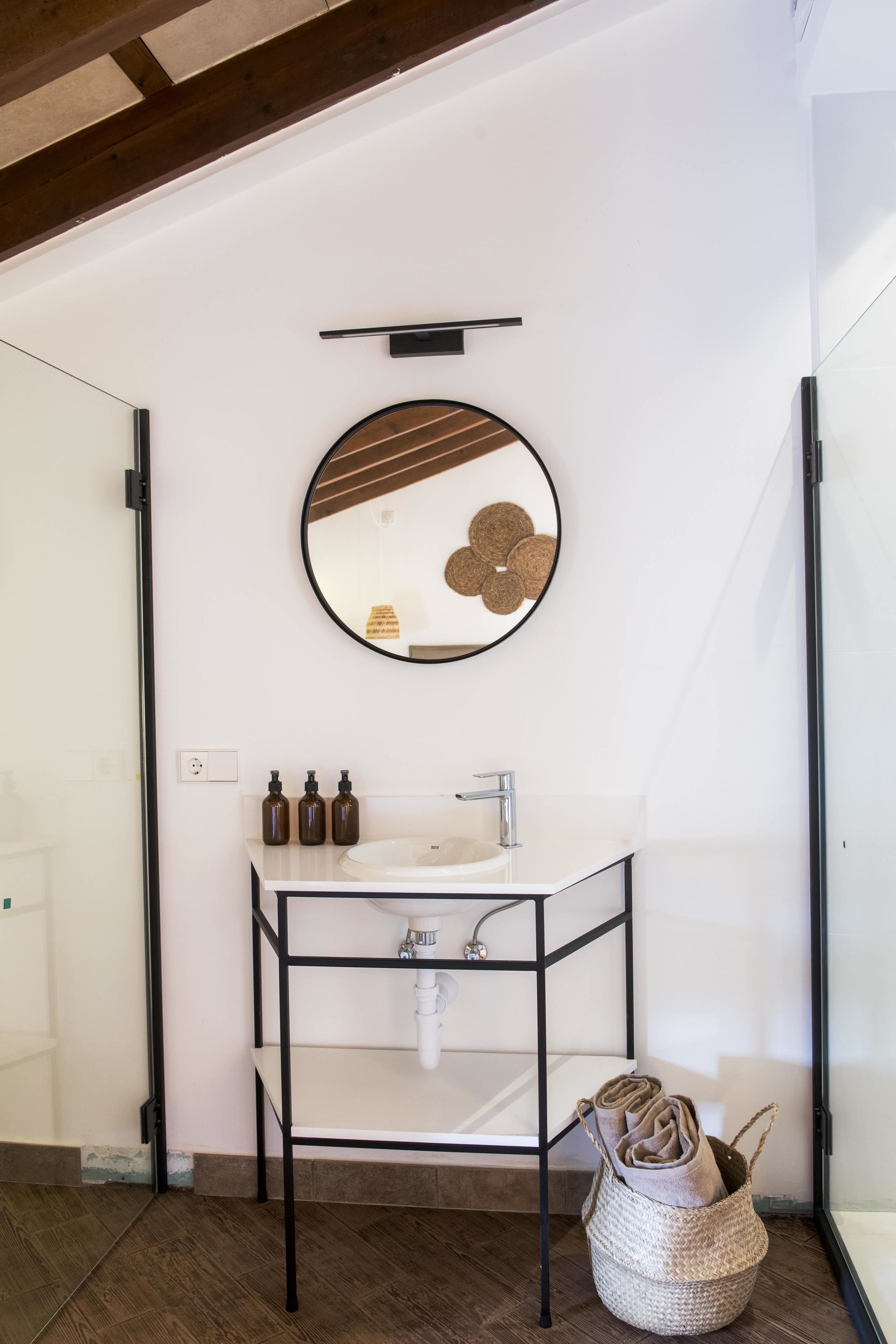 Un baño moderno con un lavamanos blanco, estante de metal negro y un espejo redondo.