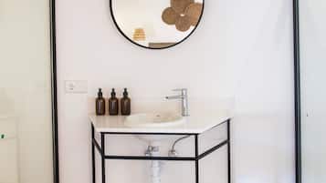 Un baño moderno con un lavamanos blanco, estante de metal negro y un espejo redondo.