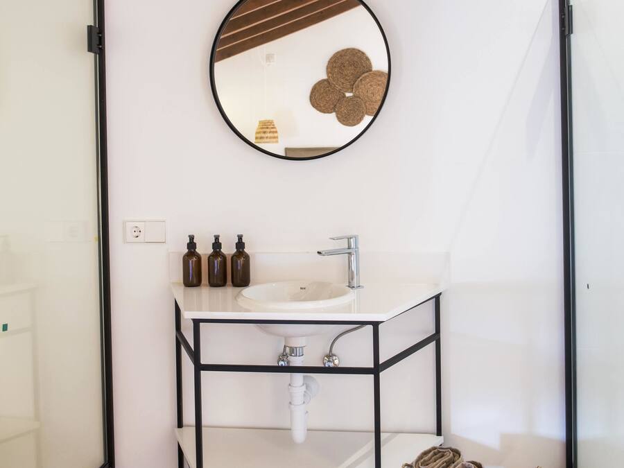 Un baño moderno con un lavamanos blanco, estante de metal negro y un espejo redondo.