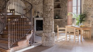 Una habitación con paredes de piedra, una escalera de caracol, una chimenea y una mesa de comedor de madera con sillas.
