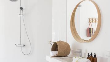 A modern bathroom with a shower, a round mirror, a sink with toiletries, and a woven basket.