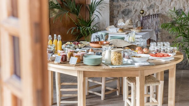 Una mesa de desayuno con diversos alimentos y bebidas, rodeada de sillas y una mesa de madera rústica.