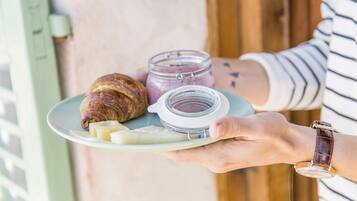 Una persona sosteniendo un plato con un croissant, queso y un frasco de mermelada.