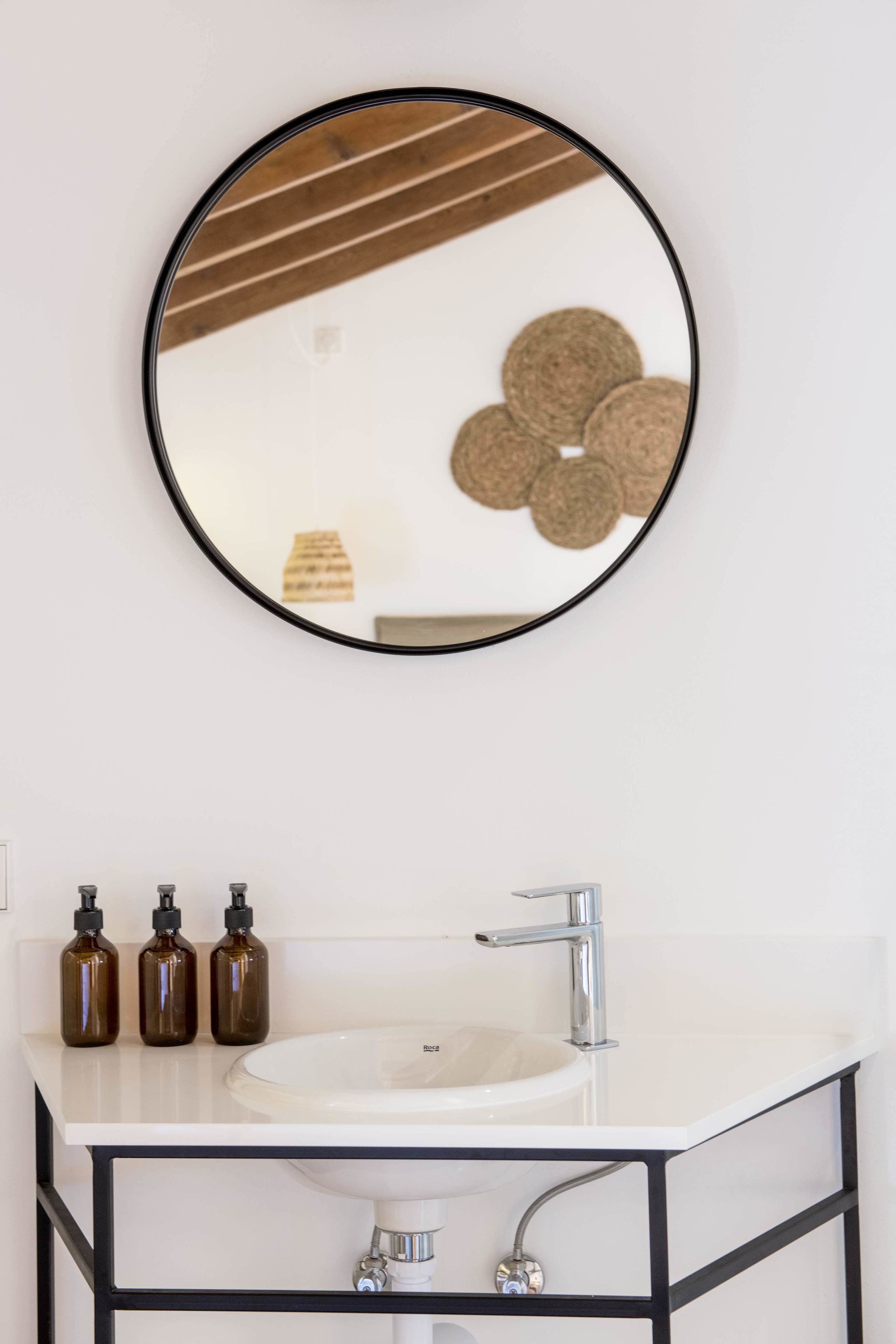 Ein Badezimmer mit einem weißen Waschbecken, einem schwarzen Metallgestell und drei braunen Flaschen auf der Ablagefläche.