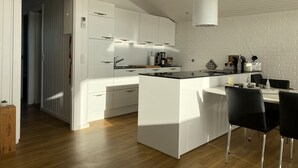 Una cocina moderna con armarios blancos, una isla central, sillas negras y una pared con diseño de ladrillo.