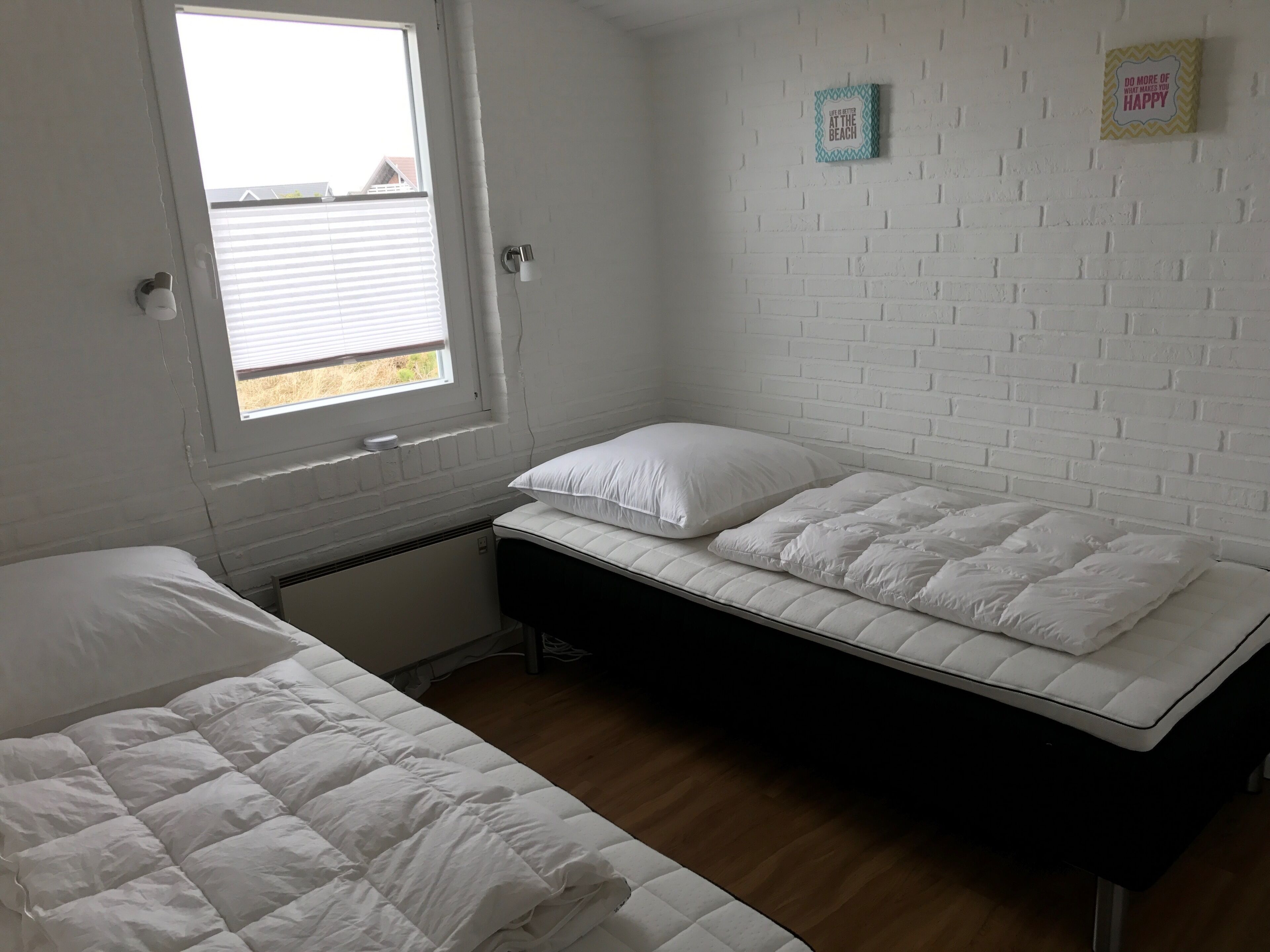 Une petite pièce aux murs blancs, avec une seule fenêtre, un lit recouvert de linge de lit blanc et un petit élément décoratif sur le mur.