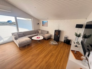 A modern living room with a sectional sofa, a round coffee table, and a fireplace. - Well-equipped summer house with a charging port for electric cars! (Hvide Sande)