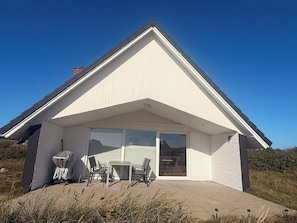 A modern house with a large glass door leading to an outdoor patio area. - Well-equipped summer house with a charging port for electric cars! (Hvide Sande)
