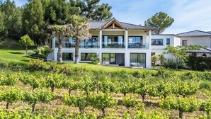 Un bâtiment à deux étages doté de grandes fenêtres, d’un balcon et d’un vignoble en premier plan.
