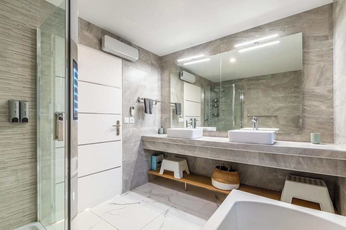 A modern bathroom with two sinks, a glass shower enclosure, and a large mirror.