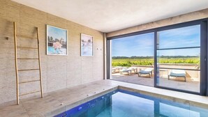 Une piscine intérieure moderne offrant une vue dégagée sur l’extérieur, avec une échelle et deux tableaux encadrés accrochés au mur.