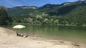A lakeside beach with a green umbrella, a sandy shore, and a backdrop of mountains.