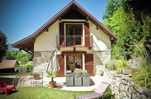 Ein zweistöckiges Haus mit Balkon, Steinmauern und einer Terrasse mit Gartenmöbeln.