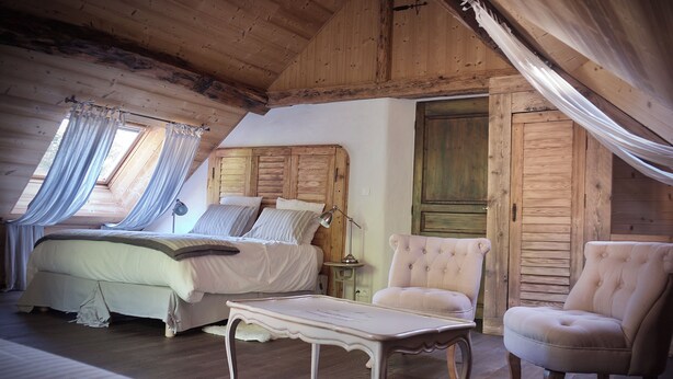 A bedroom with a bed, bedside table, two chairs, a nightstand, and a window with curtains.