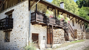 A rustic stone building with a wooden balcony, a chimney, and a staircase leading to the upper floor.