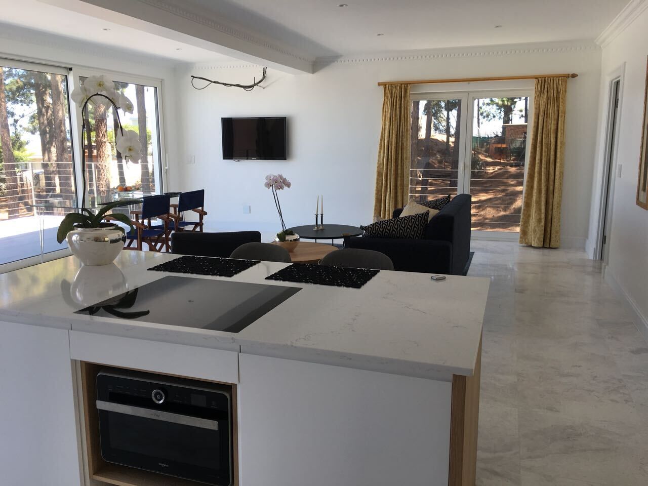 Een moderne keuken met een centraal eiland, een eethoek met stoelen, en een woonkamer met een bank.