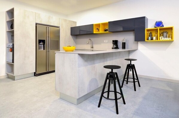 Una cocina moderna con un refrigerador empotrado, un lavamanos y dos taburetes.