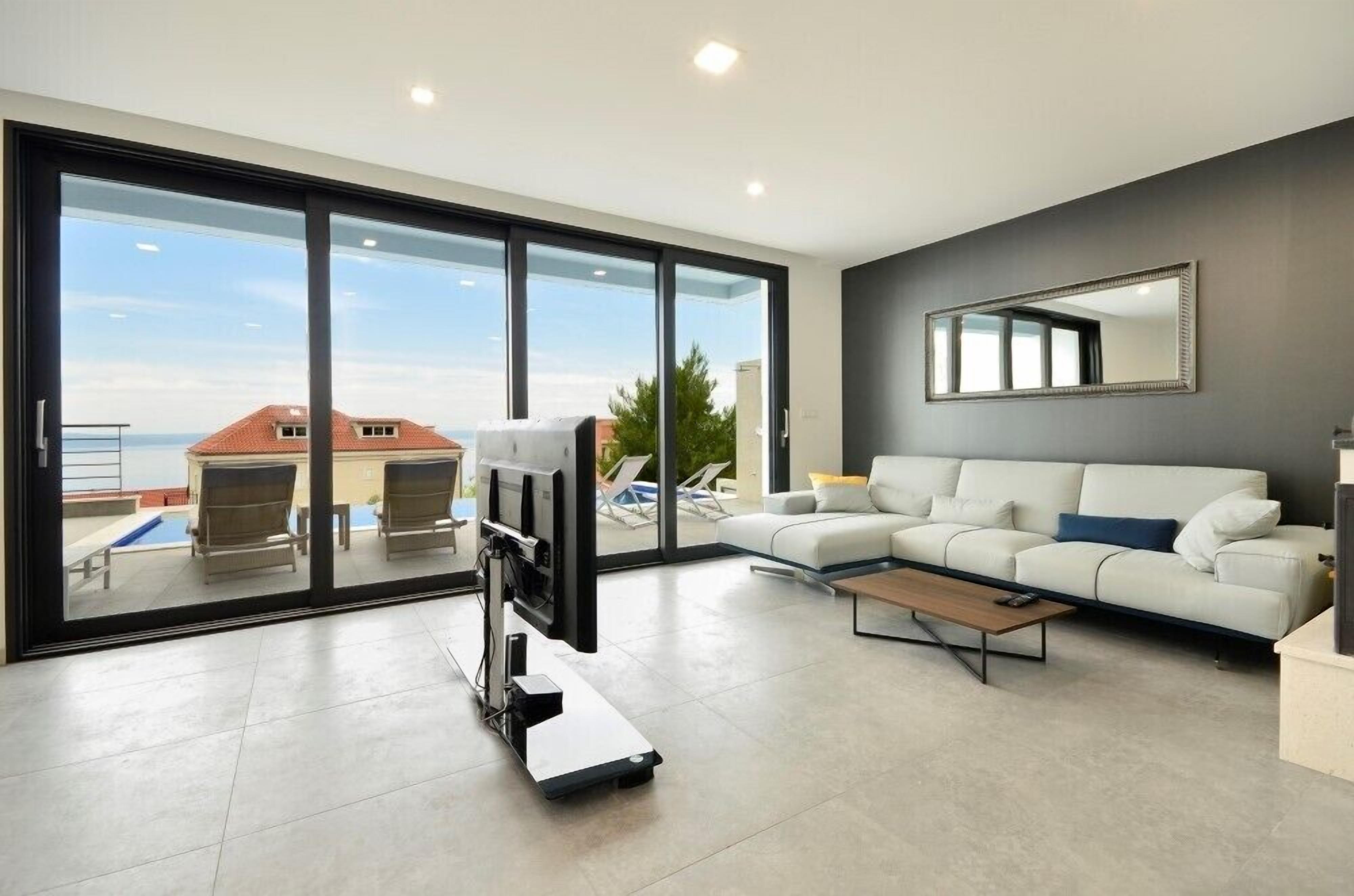 A modern living room with a large sliding glass door leading to a balcony, a white sofa, a flat-screen TV, and a minimalist coffee table.