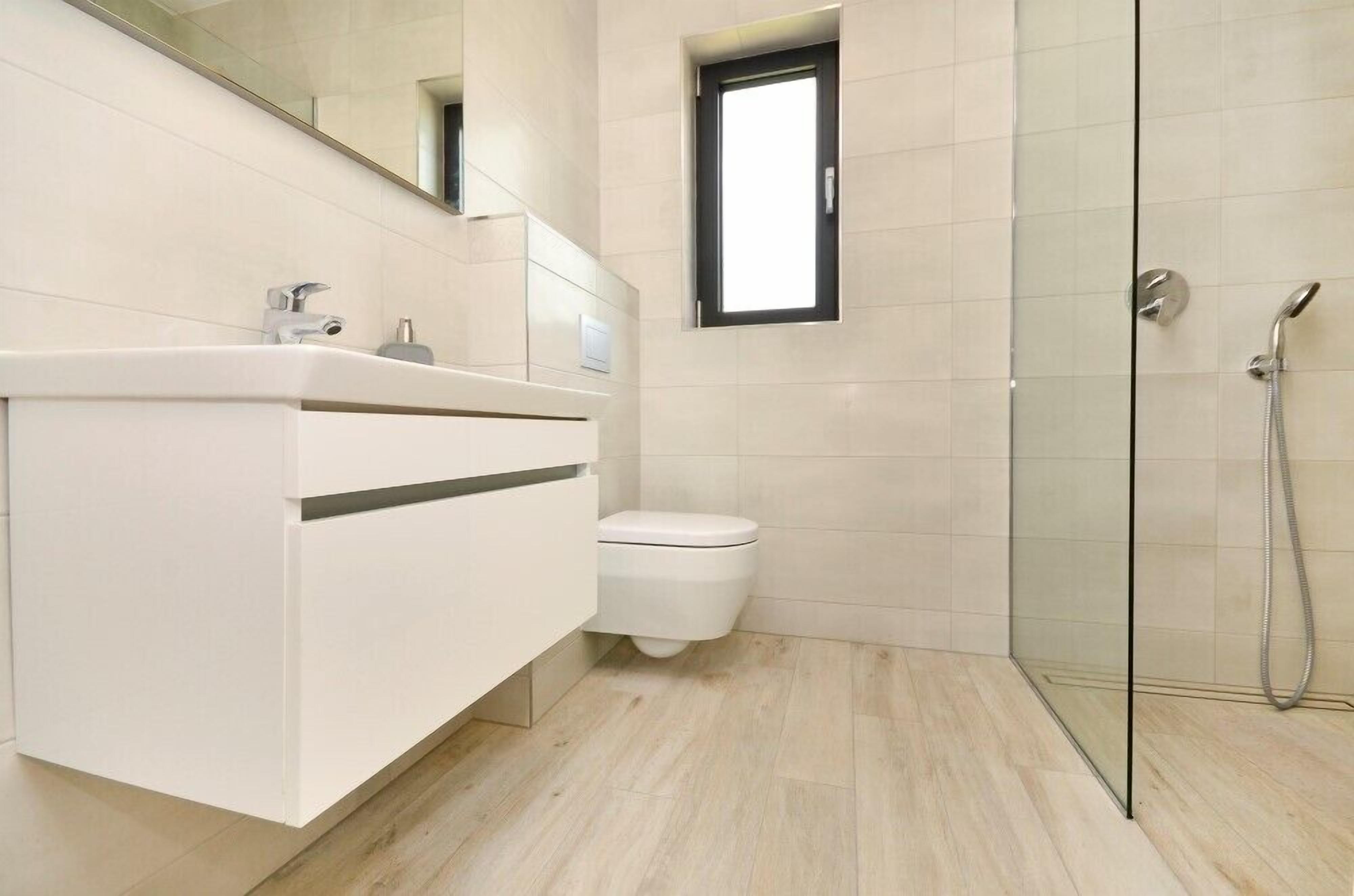 Un bagno moderno con un mobile lavabo bianco, un water e uno spazio doccia con pareti in vetro.