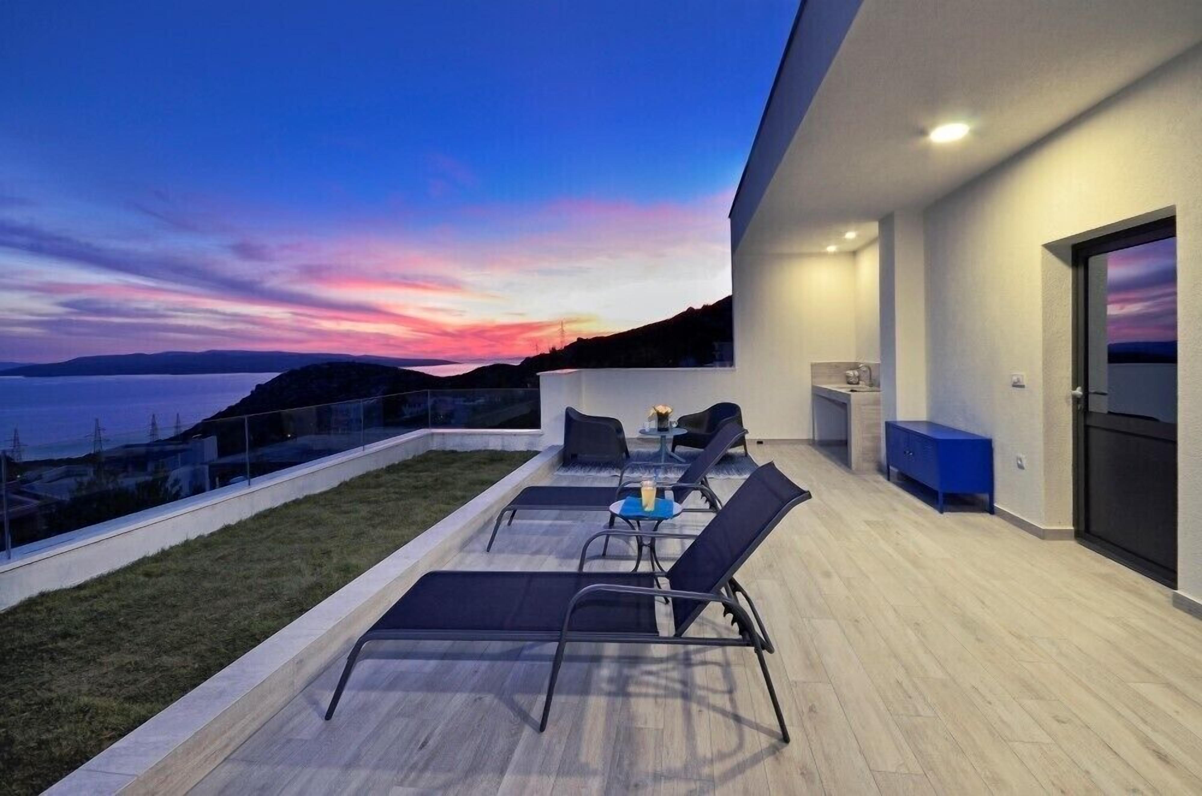 A modern outdoor terrace with lounge chairs and a table, overlooking a scenic landscape.