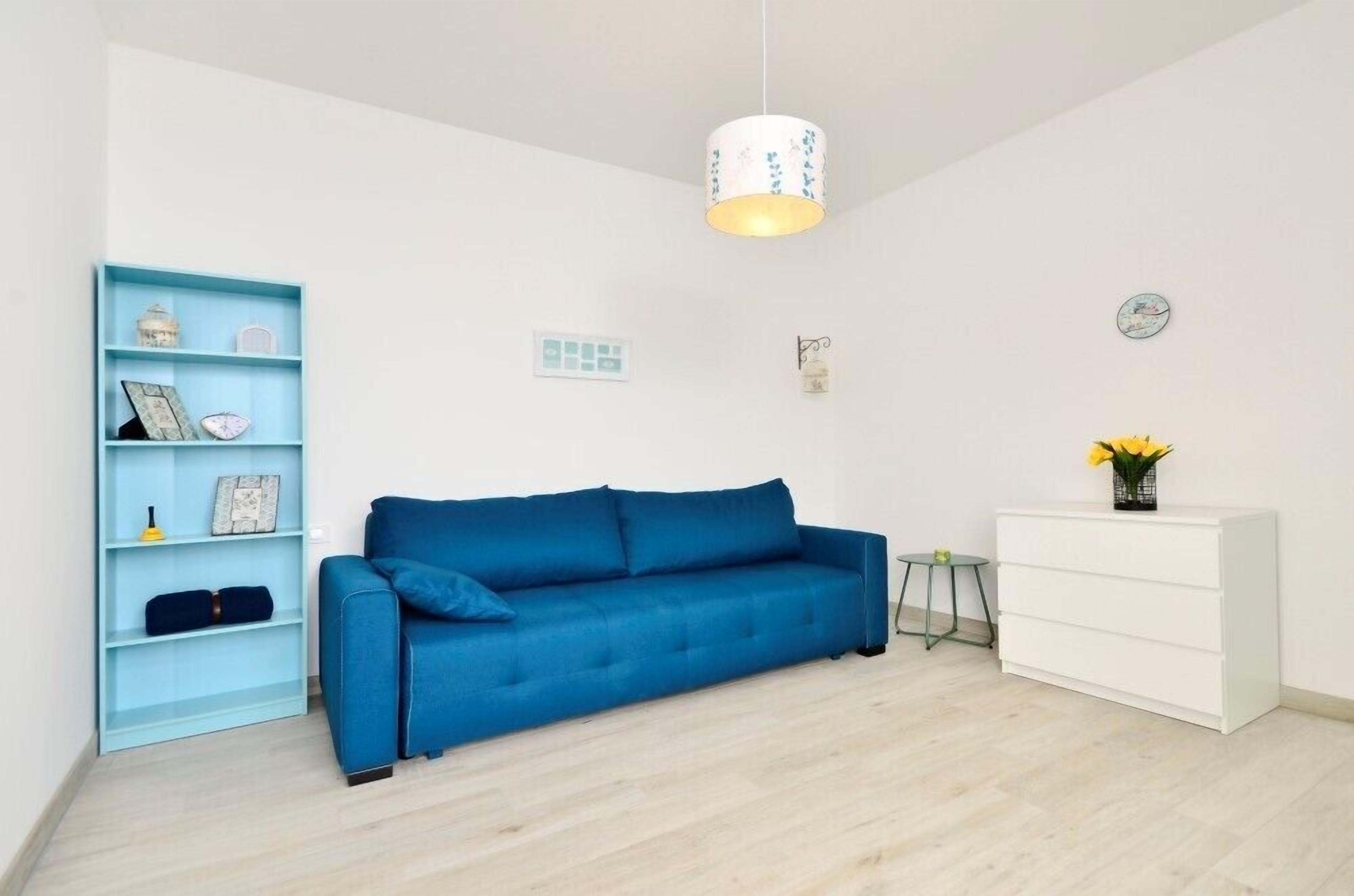 A room with a blue sofa, a white dresser, a blue shelving unit, and a hanging light fixture.