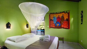 Quarto com uma cama, mosquiteiro, um quadro e um banco.