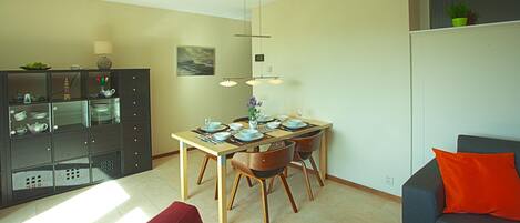 A modern living room with a dining area, featuring a sofa, a table set for four, and a cabinet with glass doors.
