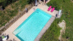 Piscina rectangular con muelle de madera, rodeada de follaje y un muro de piedra.