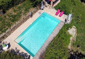 A rectangular swimming pool with a wooden deck, surrounded by greenery and a stone wall. - Comfortable 4* South-Ardèche house, airco sleeping rooms, pool, panoramic view (Chassiers)