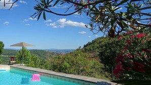 A swimming pool with a view of a mountainous landscape, surrounded by greenery and a bench.