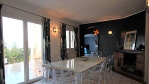 A dining area with a glass table and chairs, a fireplace, and a view through large sliding doors.