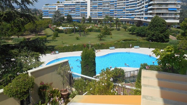 Ein Hotel mit großem Pool, üppiger Bepflanzung und einem Gebäude mit gebogenen Balkonen.