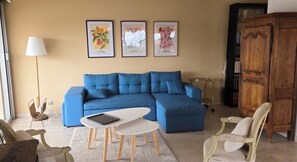 Un soggiorno con un divano blu, un tavolo bianco, una lampada e quadri appesi al muro.