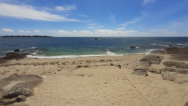 Una spiaggia con acqua cristallina, una battigia sabbiosa e rocce sparse.