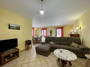 Uma sala de estar com sofá, televisão, mesa de centro e um espaço de jantar com cadeiras e mesa.