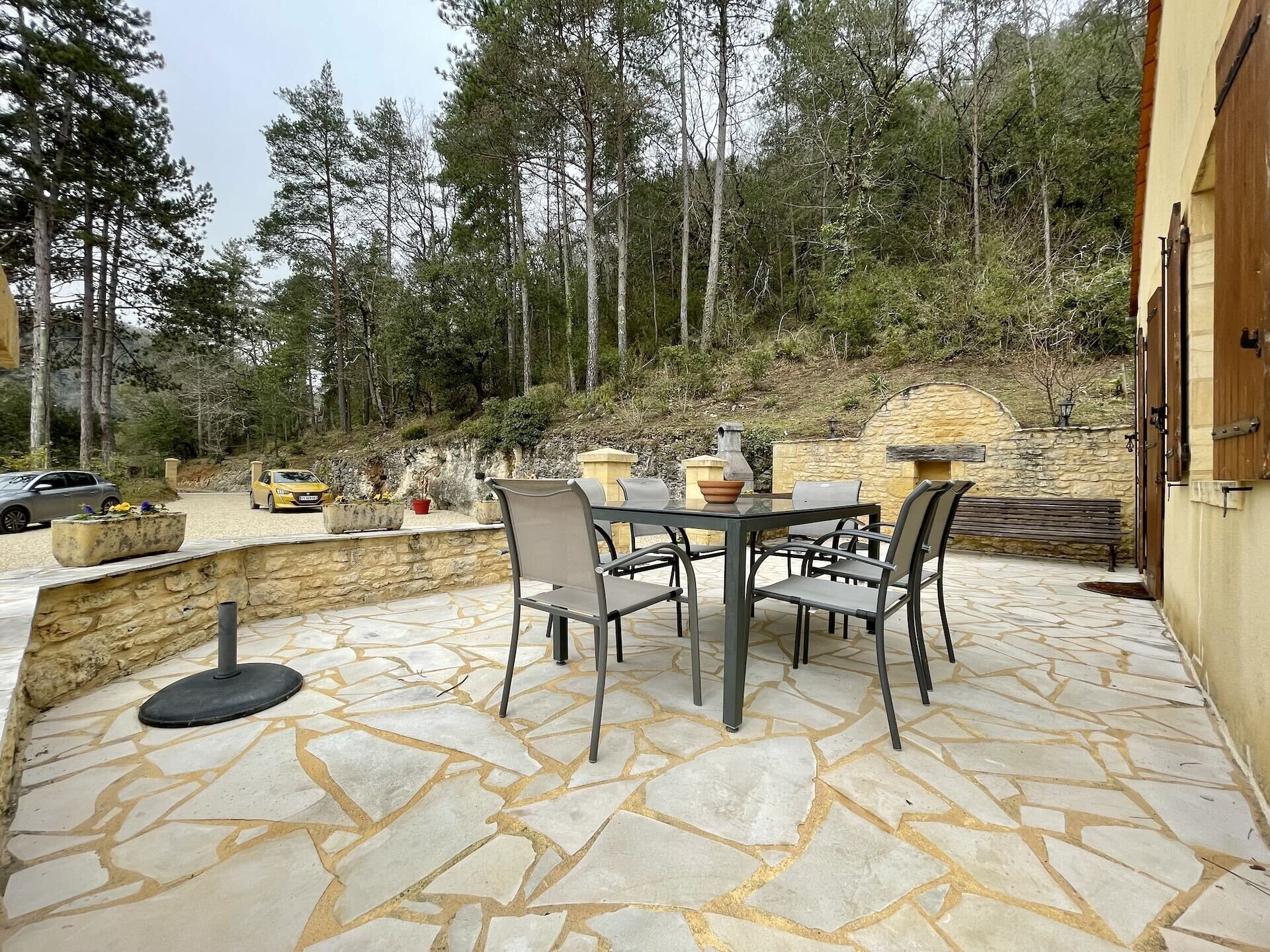 Um pátio externo com piso de pedra, uma mesa e cadeiras, e uma parede de pedra.