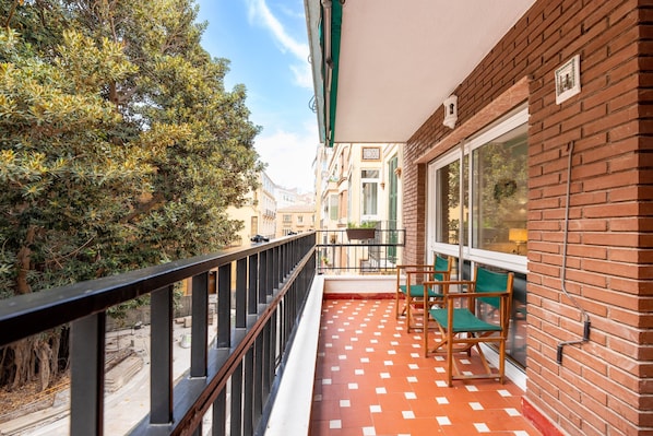 A balcony with a tiled floor, a railing, and two green chairs.