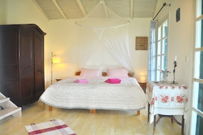 A bedroom with a canopy bed, a wooden wardrobe, a bedside table with a lamp, and a window with curtains.