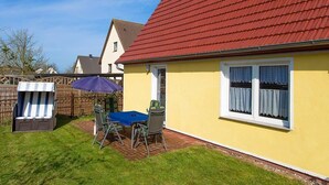 Una casa gialla con tetto rosso, un patio con tavolo e sedie, e una sedia a righe.