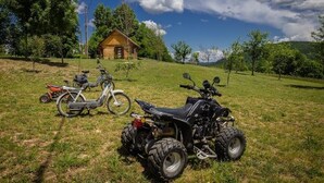 A grassy field with a wooden cabin and two ATVs parked in the foreground.