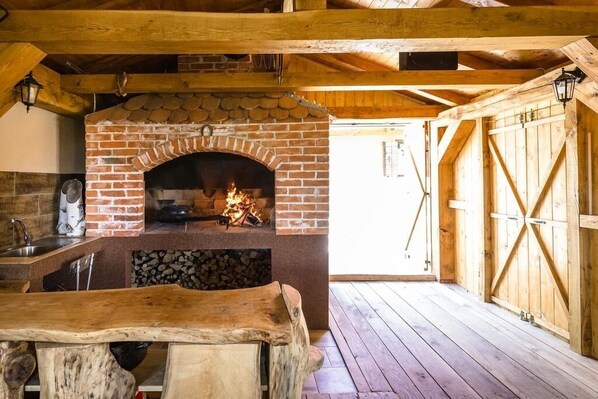 A rustic kitchen with a brick oven, wooden beams, and a wooden table.