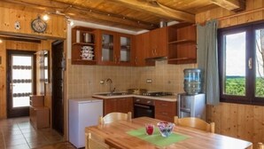 A wooden interior with a kitchen, dining area, and a view of greenery outside.
