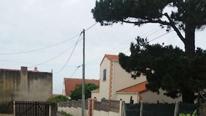 A gated driveway leading to a residential area with a house, a large tree, and a gravel path. - Single-storey house type III, 80 m from the sea and 10 mins from the town center (Préfailles)