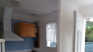 A compact kitchen with wooden cabinets, a white stove, and a window with lace curtains. - Single-storey house type III, 80 m from the sea and 10 mins from the town center (Préfailles)